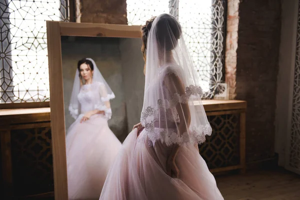 Die Braut versammelt sich am Morgen vor dem Spiegel. die Braut versammelt sich am Morgen. stilvolles rosa Hochzeitskleid. die Braut dreht sich in einem Kleid neben dem Spiegel. — Stockfoto