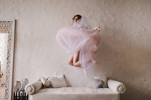 La novia salta al sofá. La novia se reunirá por la mañana. Elegante vestido de novia rosa . — Foto de Stock