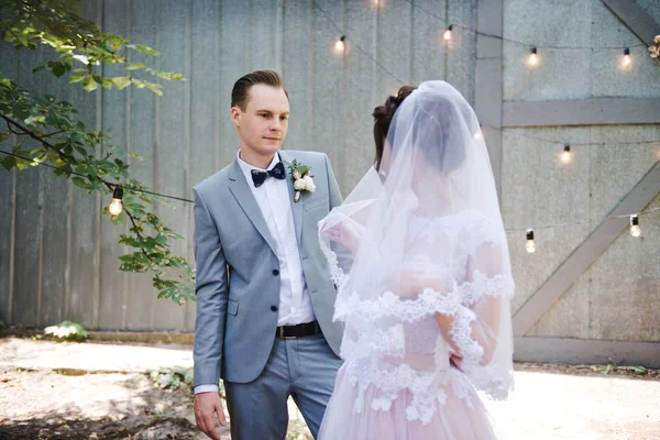 Hochzeit. Porträt einer schönen Braut und Bräutigam. Vor dem Hintergrund einer Girlande aus Glühbirnen und Metalltüren spazieren Braut und Bräutigam durch den Garten. Strauß von Grün und Blumen. — Stockfoto