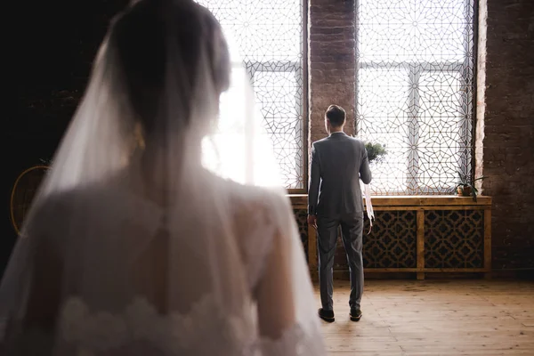 Der Bräutigam wartet im grauen Anzug auf die Braut. Bräutigam hält Blumenstrauß und wartet auf Braut. Hochzeitstag. der Bräutigam steht neben einem großen Fenster. — Stockfoto