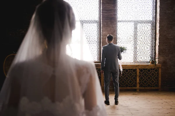 El novio está esperando a la novia con un traje gris. Novio sosteniendo ramo y esperando a la novia. Día de la boda. El novio está cerca de una gran ventana . — Foto de Stock