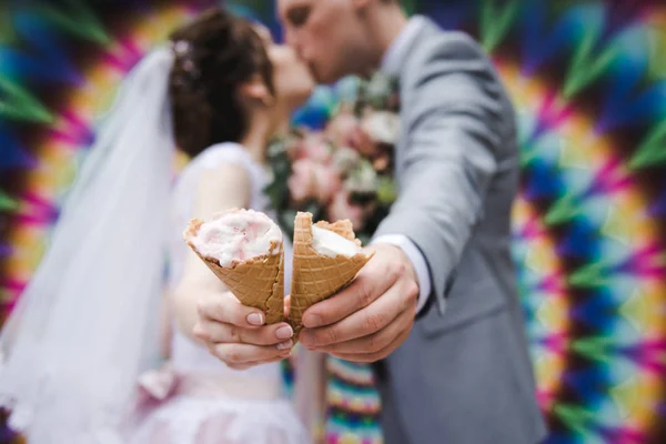 新郎新婦は明るい壁の背景に一緒にアイスクリームを食べています。面白い新婚夫婦はアイスクリームを食べる。ハッピーウェディングデー — ストック写真