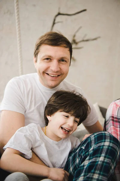 Un bel homme et son fils. La fête des pères. Père et fils en pyjama sont assis dans un lit. Père heureux avec fils jouant à la maison sur le lit, temps heureux . — Photo