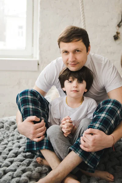 英俊的男人和他的儿子。父亲节穿着睡衣的父亲和儿子正坐在床上。快乐的父亲与儿子在家里玩在床上,快乐时光. — 图库照片