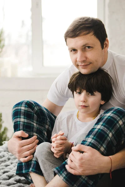Un bel homme et son fils. La fête des pères. Père et fils en pyjama sont assis dans un lit. Père heureux avec fils jouant à la maison sur le lit, temps heureux . — Photo