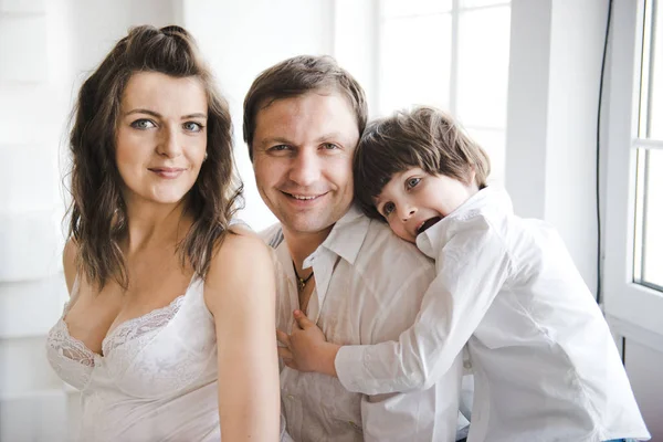 Une famille heureuse attend un deuxième enfant. Femme enceinte avec mari et petit garçon. Deuxième grossesse, concept de maternité. Joyeux famille près de la fenêtre. Fond blanc . — Photo