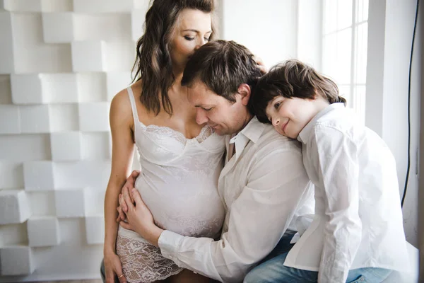 Une famille heureuse attend un deuxième enfant. Femme enceinte avec mari et petit garçon. Deuxième grossesse, concept de maternité. Joyeux famille près de la fenêtre. Fond blanc . — Photo