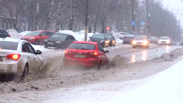 Floresta de neve na cidade, o fluxo de carros dirigindo na estrada através de uma poça — Vídeo de Stock