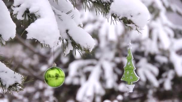 Neve cai no inverno na floresta, ramo com um brinquedo de Natal oscila no vento — Vídeo de Stock