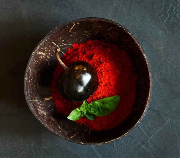 Chili peper poeder met basilicum in schaal op grijze achtergrond Stockfoto