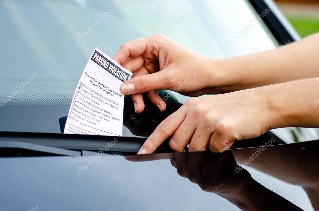 Close-up Of A Woman Taking Parking Ticket On Car's Windshield