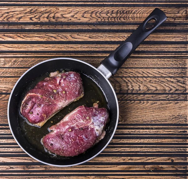 Raw duck breast in round frying-pan on wooden background. Raw fresh meat. Beef steaks in round frying pan on wooden background