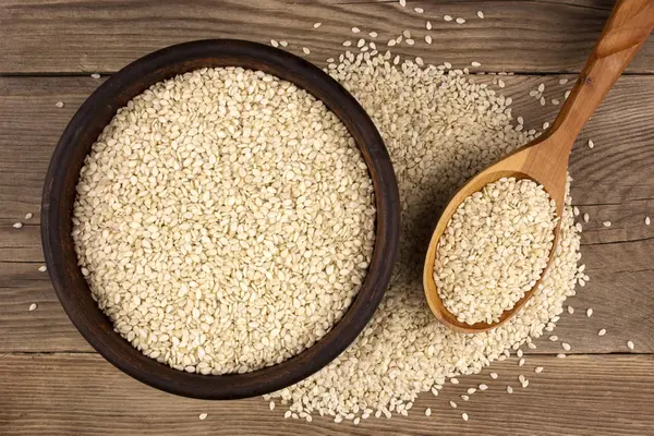 Bir kase bir tahta kaşıkla ahşap arka plan üzerinde beyaz susam