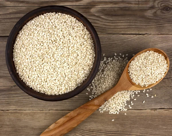 Bir kase bir tahta kaşıkla ahşap arka plan üzerinde beyaz susam