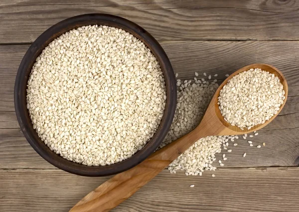 Bir kase bir tahta kaşıkla ahşap arka plan üzerinde beyaz susam