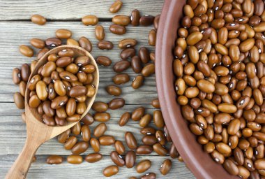 Tahta kaşıkla ahşap masa üzerinde seramik kase kuru fasulye. Üstten görünüm