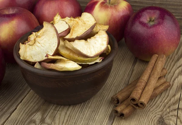 Bowl with dried apple, on an old wooden table with fresh apple and cinnamon.