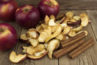 Ev yapımı kurutulmuş organik elma dilimleri, taze elma ve tarçın ile eski bir ahşap masa.