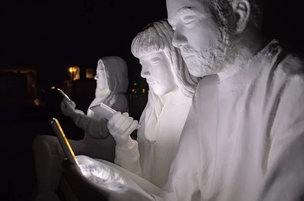 White sculptures of people looking at phone at amsterdam light festival