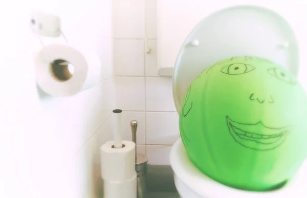 green balloon with painted face on a toilet