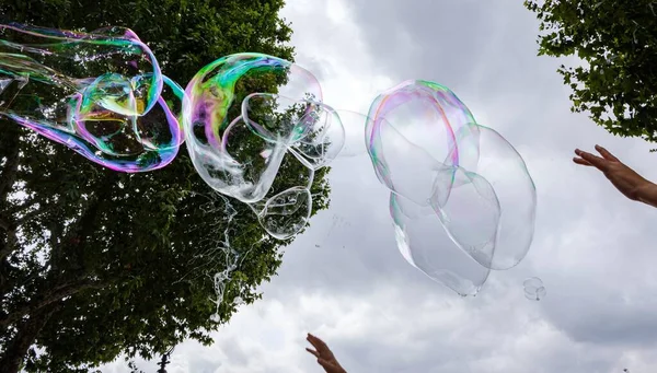 giant soap bubbles explode at the touch of children's hands against a cloudy sky with trees