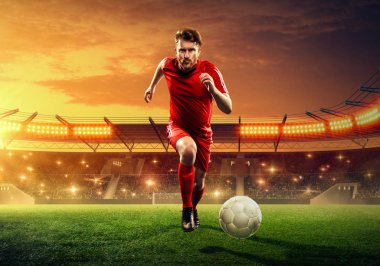 Futbolcu bir oyun sırasında bir stadyumüzerinde bir top top salya. Dramatik gece gökyüzü ile ışıklandırılmış gece futbol stadyumu