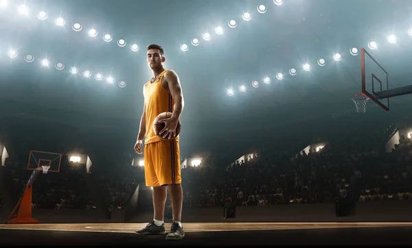 Basketball player in sports uniform with a ball on a floodlit basketball arena