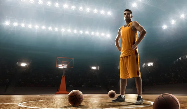 Basketball player in sports uniform with a ball on a floodlit basketball court