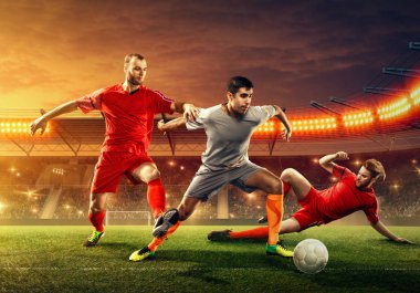 Üç futbolcu taraftarlar cheeering ile profesyonel stadyumda oyun sırasında bir top için mücadele