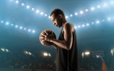 Professional african american basketball player in sports uniform with a ball on a floodlit basketball court fully concentrated before the game clipart