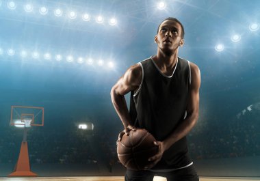 Young professional african american basketball player with a ball on a floodlit basketball arena clipart
