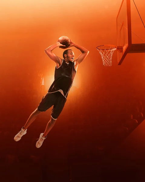 African american basketball player in sports uniform on a professional basketball court in action with the ball. Slam dunk. Jump shot. Red floodlit background