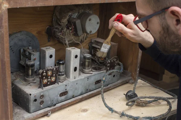 Man is dusting old radio vintage radio with a brush.