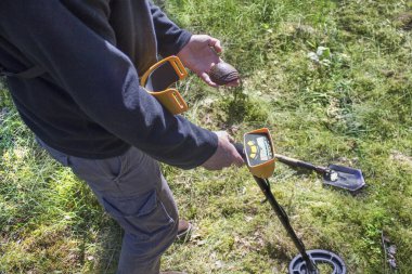 Dünya Savaşı'ndan gelen memorabilia için arama. Bir adam bir bomba üzerinden sigorta gösterir. Dedektör bobin ve arka planda kazmacı.