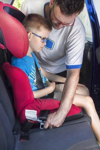 The man fastens a seat belt to a child who is sitting in a car seat in the back seat. Father buttoning the seat belt to his son who is sitting in the car seat in the back seat of the car.