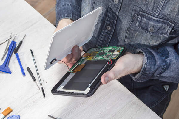 The electronic service employee holds the tablet's integrated circuit in his hands. Work station in an electronic service. Tablet repair.