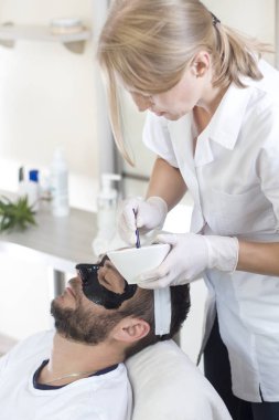 Güzellik Salonu. Şevval özçelik güzellik adamın yüzünü bir fırça ile siyah bir maske koyar. Erkek Bakımı, Kozmetik tedavi sırasında güzellik salonda bir adam.