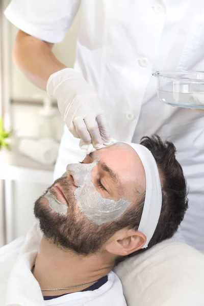 The hands of a beautician in disposable gloves wash the man face with cotton swabs