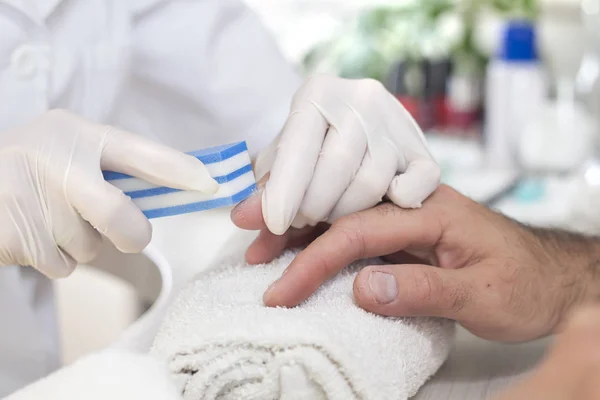 Beautician in white disposable gloves in a beauty salon during a manicure treatment manicures his nails with a nail file in the palm of a man