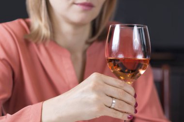 Bir kadın eli kırmızı çivi ve bir nikah yüzüğü parmağına ile bir bardak şarap tutar.