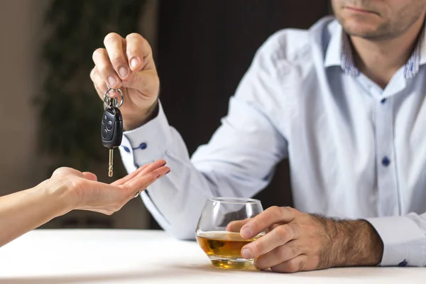 Do not drink, do not go. A man in a bright shirt is sitting at the table with a glass of whiskey. He gives the woman the keys to the car.