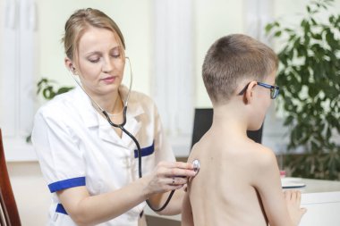 Tıbbi muayene sırasında kadın akşam doktor. O doktor ofisinde bir stetoskop ile çocuğun akciğerlere dinler.