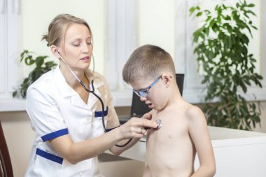 Child during medical examination in the office of a pediatrician. Medical examination with a chest stethoscope in a doctor's office. The boy with open mouth breathes deeply. clipart