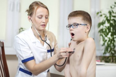 Child during medical examination in the office of a pediatrician. Medical examination with a chest stethoscope in a doctor's office. The boy with open mouth breathes deeply. clipart