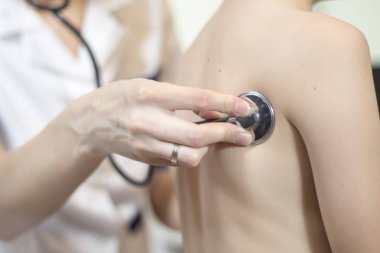 Tıbbi muayene sırasında çocuğun göğsüne bağlı stetoskop baş doktorun elini tutar.