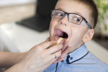 A boy with open-mouth during a medical examination. The doctor checks the throat and tonsils of the patient using a wooden spatula. clipart