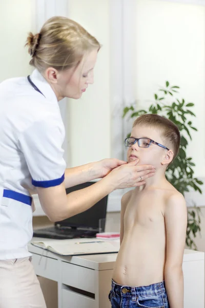医生在医生的办公室 同时检查一个戴眼镜的男孩的扁桃体 — 图库照片