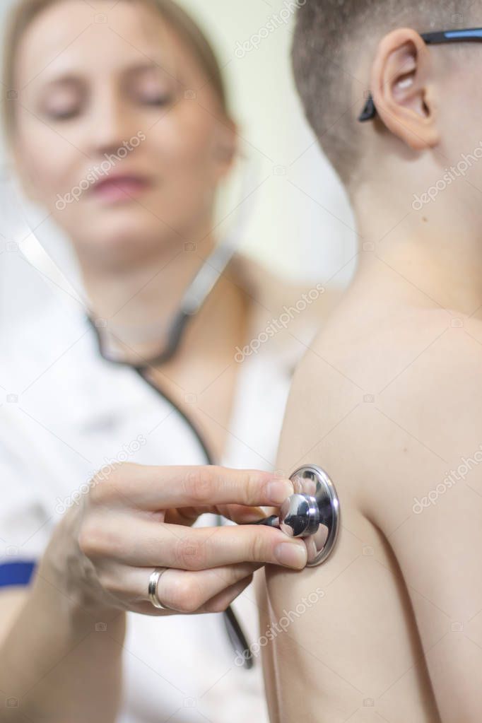 The doctor's hand holds the stethoscope head attached to the child's chest during the medical examination.