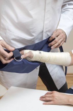 Ortopedi uzmanı Doktor bir askı bandajlı kadının el koyar.