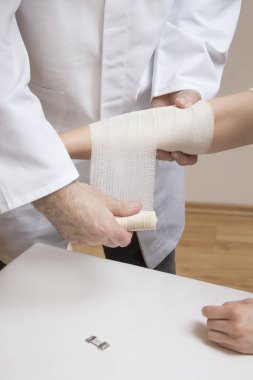 The doctor puts a dressing from the bandage on the woman's forearm.